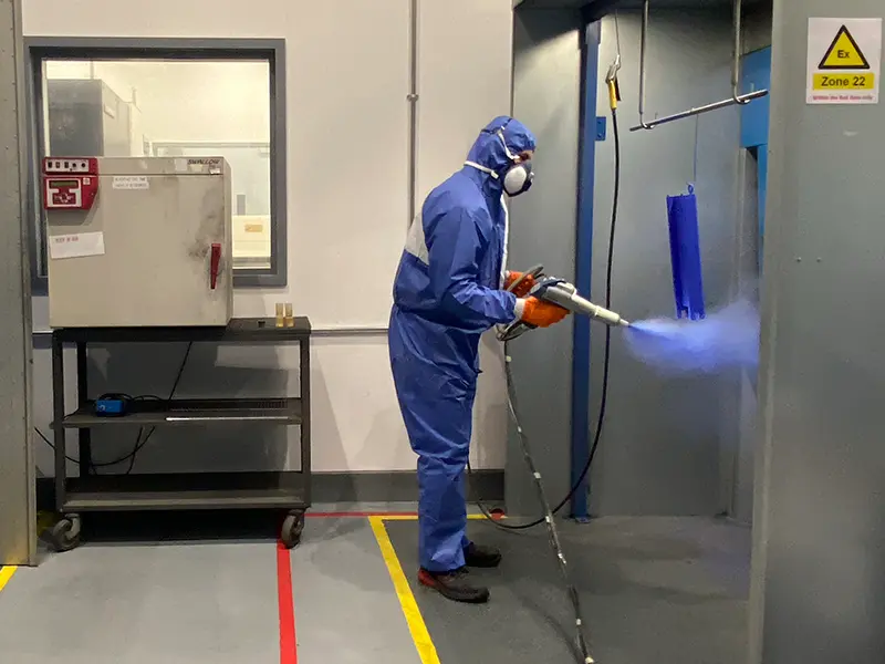 Man spraying powder coating metal component in spray booth